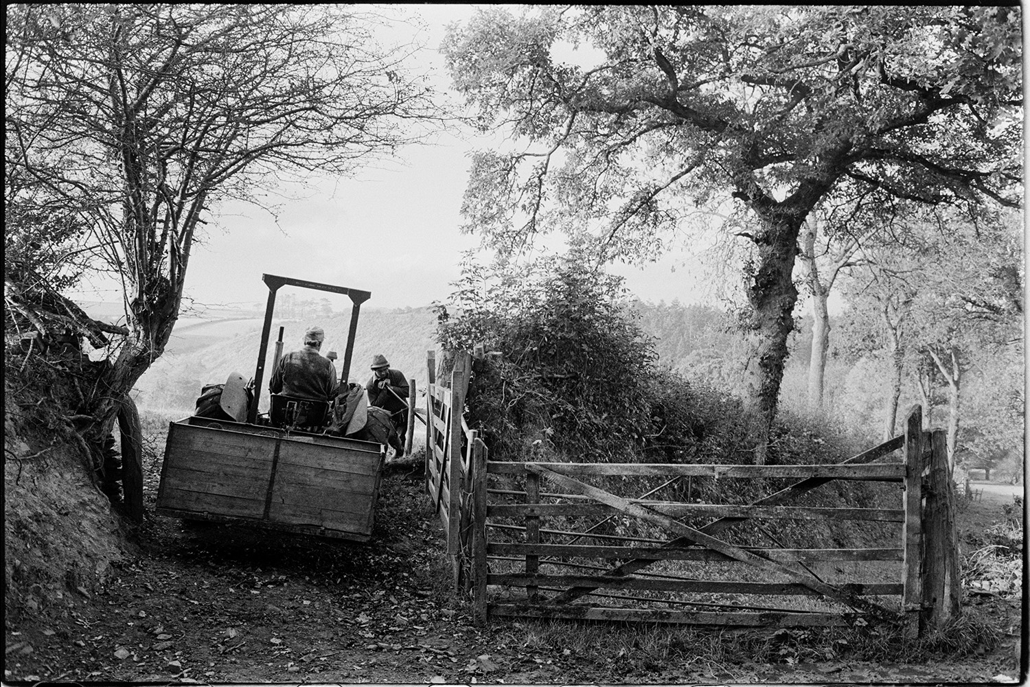 Farmers mending fencing. 
[Alf Pugsley driving a tractor and link box through an open field gateway at Lower Langham, Dolton. Stephen Squire is holding back part of the gate or fence by the field entrance.]