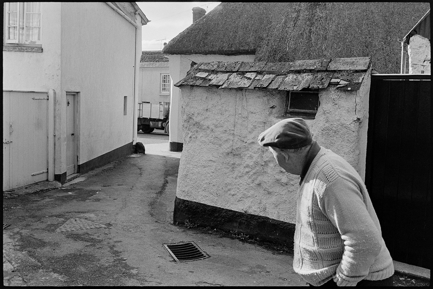 Back lane with cob walls. 
[Cob and thatch buildings in Buddle Lane, Hatherleigh. A man is watching Hatherleigh Carnival from the lane.]