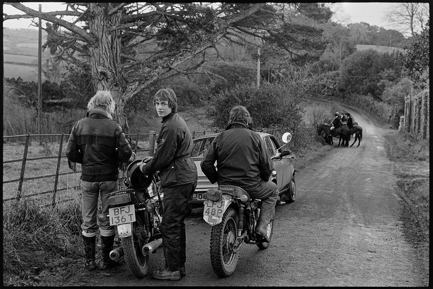 Hunters, horses and followers waiting for a scent, listening for hounds. 
[Hunt followers on motorbikes and in a car in a lane at Halsdon, Dolton. They are watching huntsmen on horses further down the lane.]