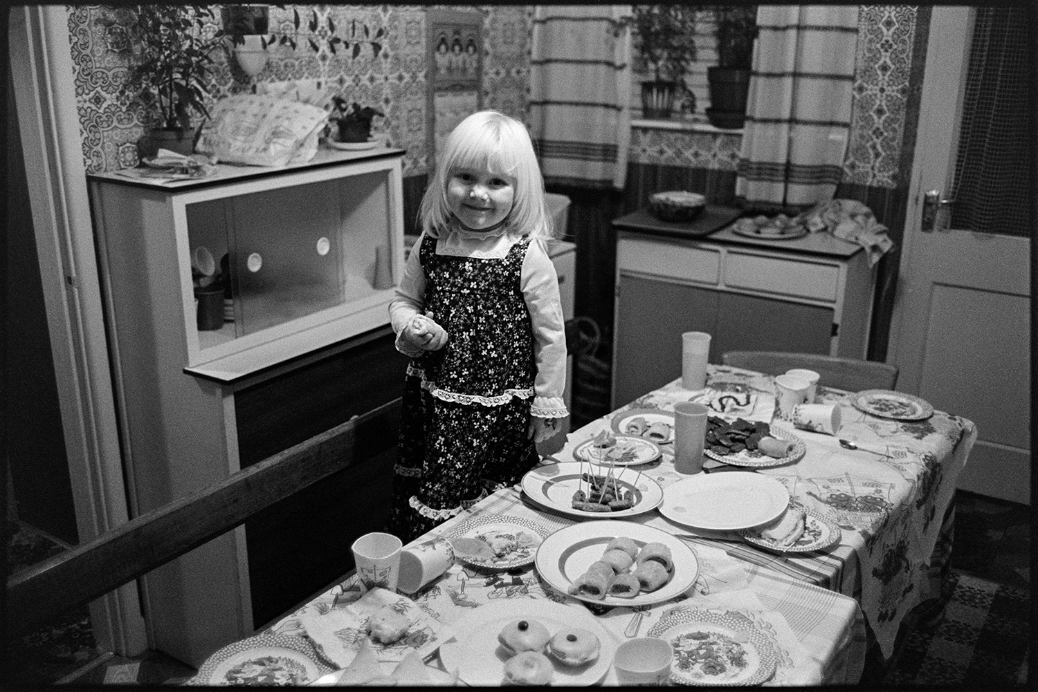 Children's party food on table. Birthday Party. 
[Rachel Davey at a children's birthday party in a house at Rectory Road, Dolton. She is stood on a bench by a table laid with party food.]