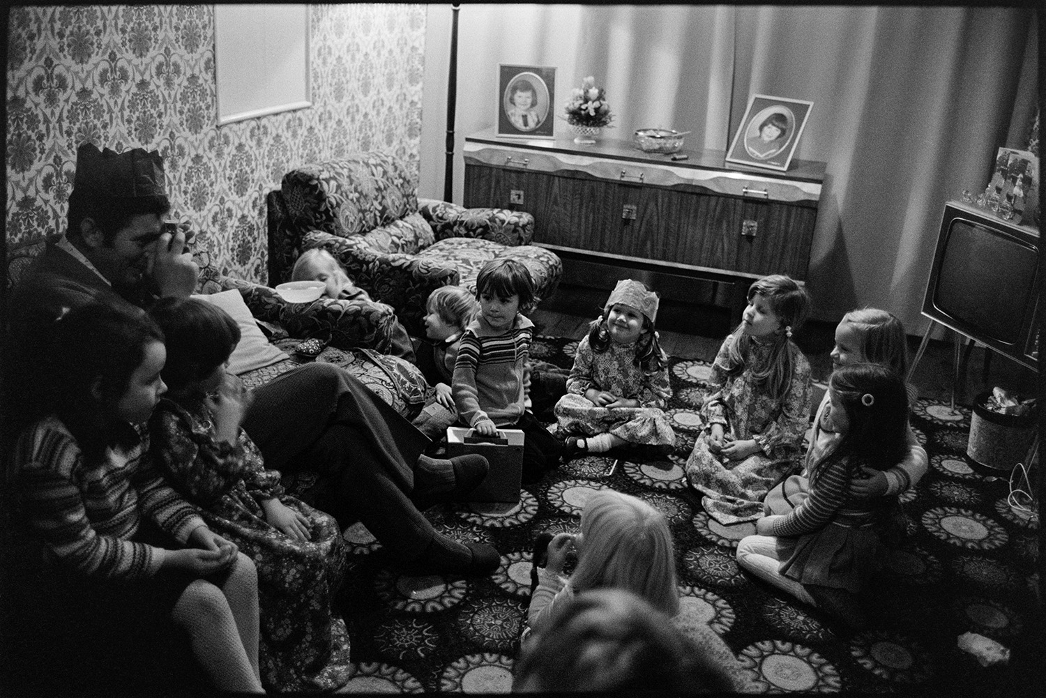 Children's party food on table. Birthday Party. 
[Children playing party games at a birthday party in the living room of a house at Rectory Road, Dolton. A man is taking a photograph of some of the children. A television and sideboard with photographs are visible in the background.]
