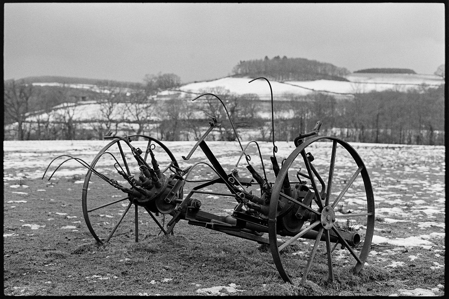 Snow, old whisk, abandoned in field. 
[An old hay whisk in a snowy field at Ashwell, Dolton.]