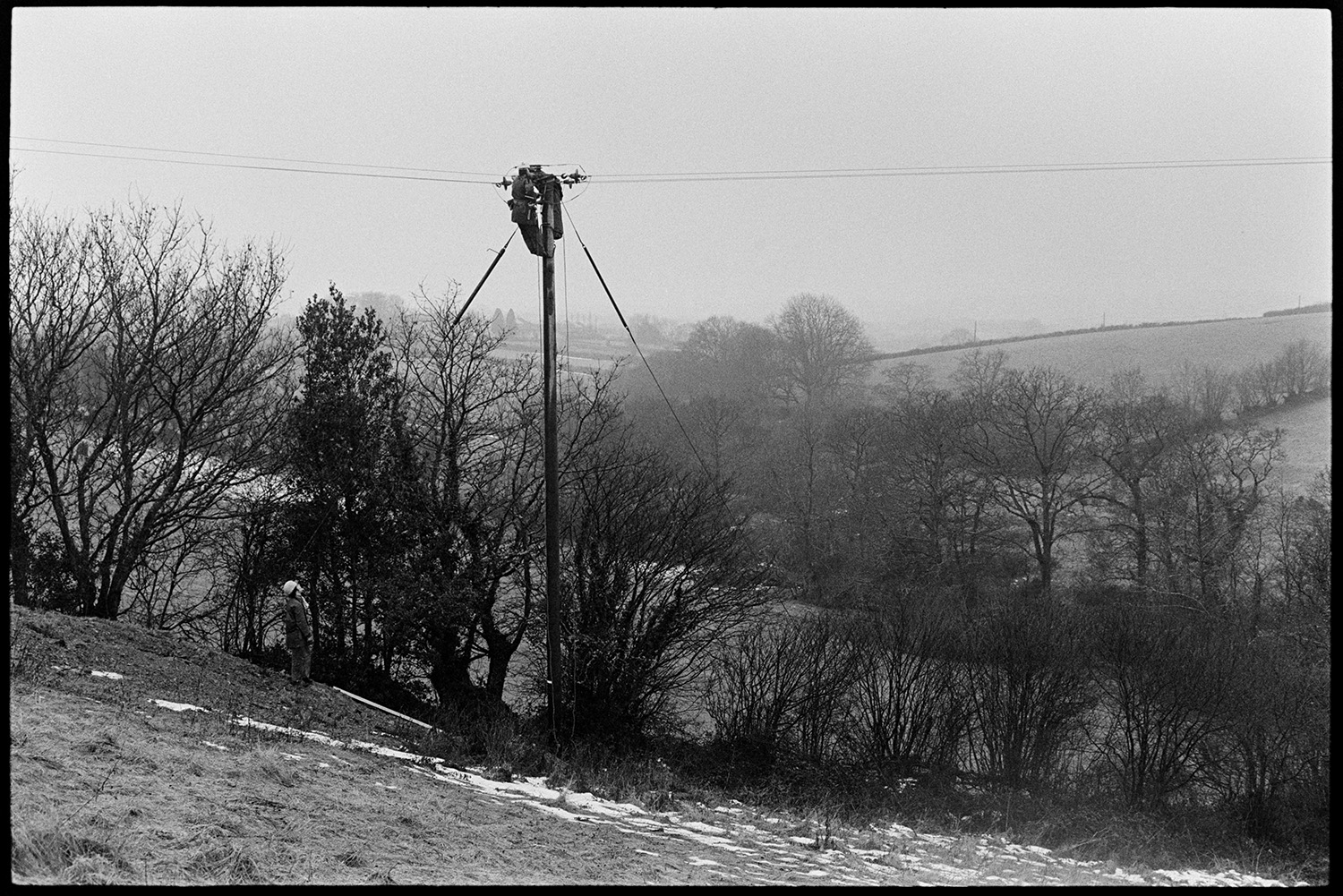 Men replacing electricity power lines, Land Rover and drums of cable. 
[A utility pole in a field at Dolton supporting electricity power cables. Patches of snow can be seen in the field.]