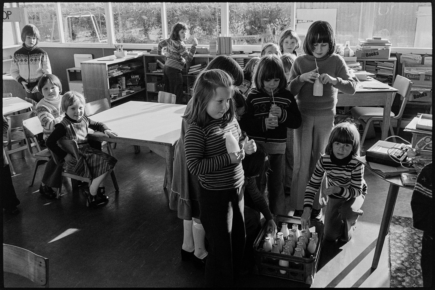 Primary school classroom with headmistress teaching, views of full classroom. 
[Schoolchildren taking their bottles of free milk from a crate, in a classroom at Burrington Primary School.]