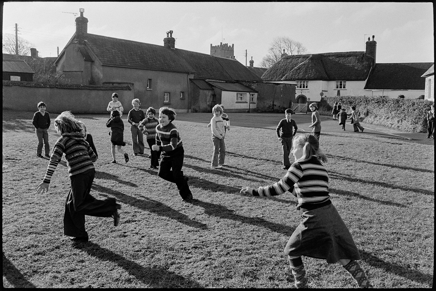 School children playing in playground and on village green, the kitchen. 
[Schoolchildren playing on the village green at Burrington. The thatched Barnstaple Inn can be seen in the background.]