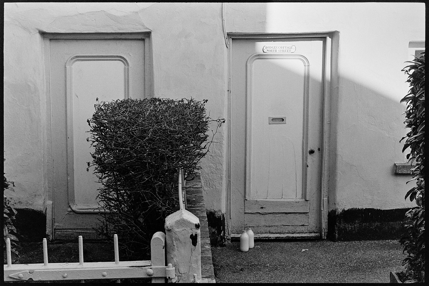 Man taking in his milk, two interesting doorways, one blocked. 
[Two milk bottles outside the front door of Hodges Cottage, North Street, Dolton, where Harold Pickard lived, also known as Argo Pickard. The door of the adjacent cottage is blocked.]